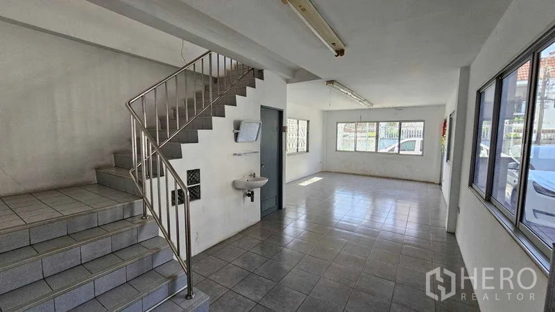 Warehouse for rent in Lak Si, Bangkok - Bright ground-floor warehouse office with tiled flooring, staircase, and large windows.