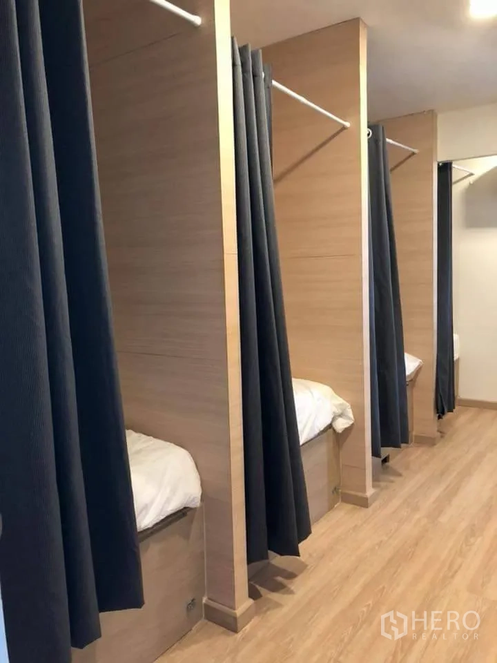 Detached House for rent in Watthana, Bangkok - Row of built-in sleeping pods with privacy curtains along a wood floor corridor.