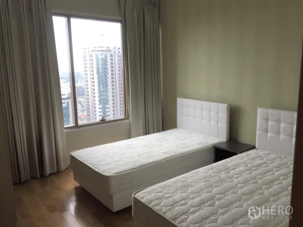 Condominium for rent or sale in Khlong Toei, Bangkok - Twin bedroom with large window, city skyline view, wood flooring, and neutral curtains.