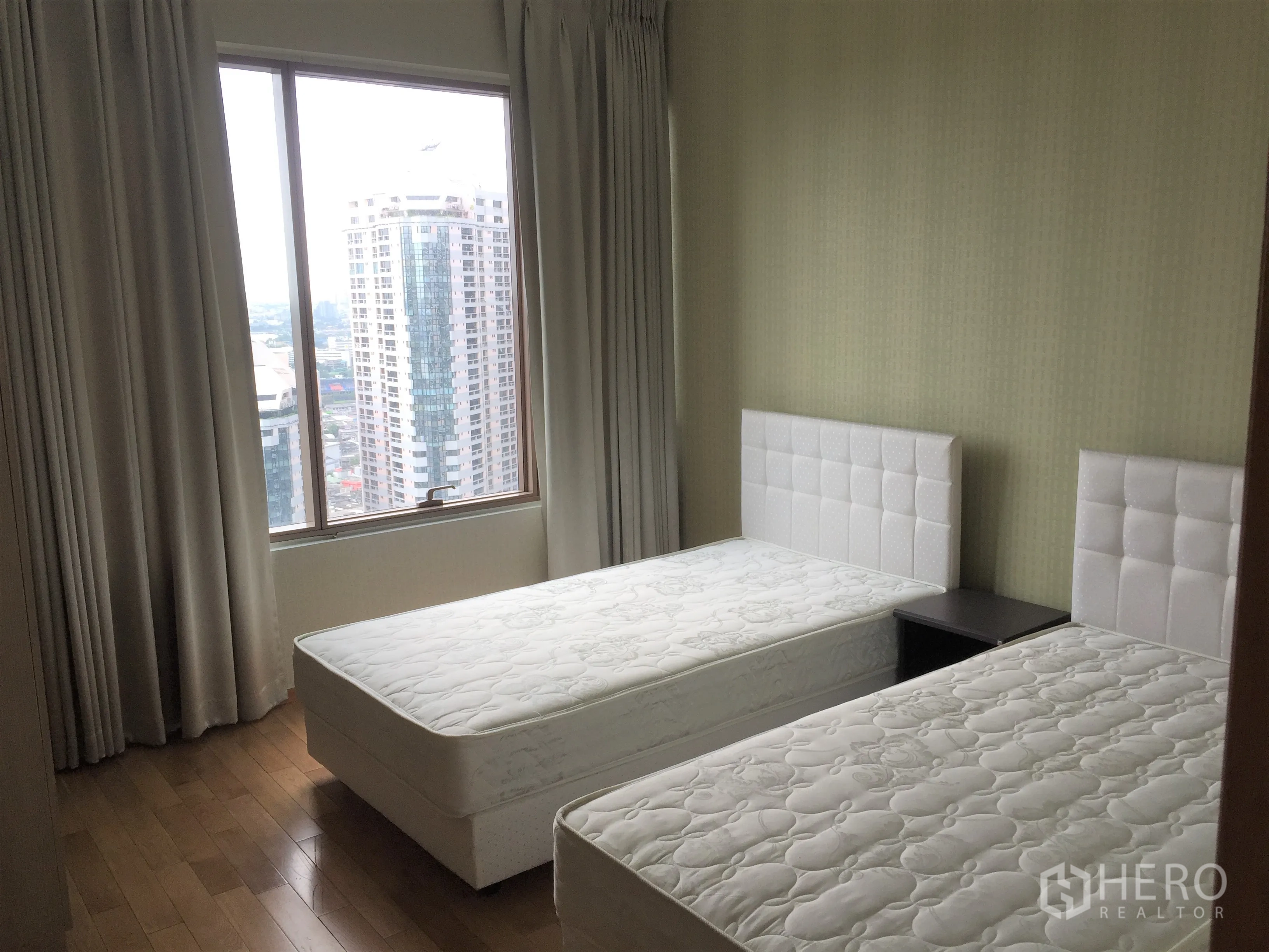 Condominium for rent or sale in Khlong Toei, Bangkok - Twin bedroom with large window, city skyline view, wood flooring, and neutral curtains.