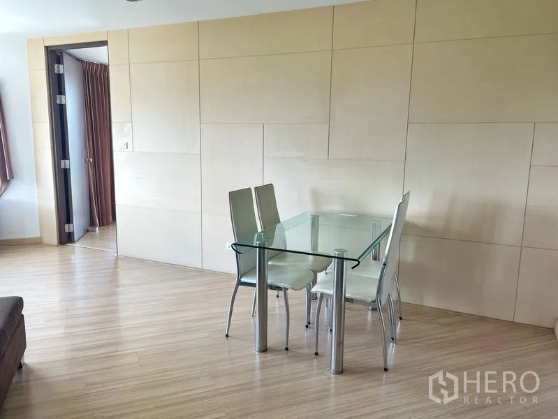 Condominium for rent in Khlong Toei, Bangkok - Glass-top dining table with four chairs against a light feature wall and wood floors.