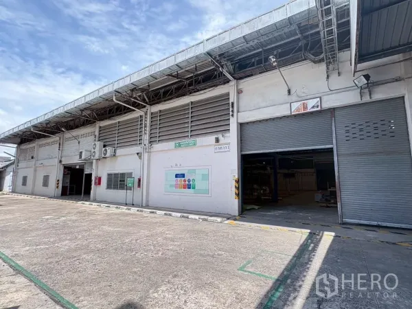 工厂 出租或出售在Bang Khun Thian, Bangkok - 曼谷邦昆天区工厂外观，多个卷闸门与宽阔车道，蓝天下全景。