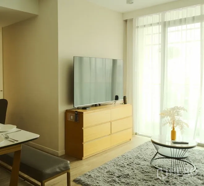 Condominium for rent in Bang Rak, Bangkok - Living area with smart TV on wooden console, round coffee table and natural light.