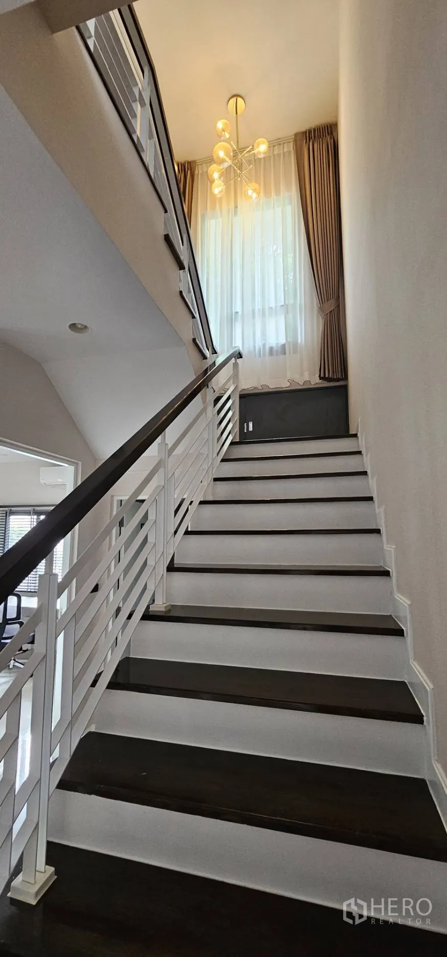 Detached House for rent in Bang Kapi, Bangkok - Staircase with wood steps and a chandelier below a tall window.