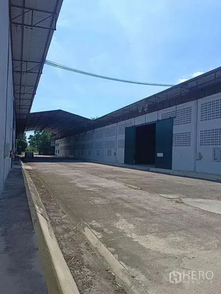 货栈 出租在Mueang Rayong, Rayong - 外部装卸通道，长条仓库立面与绿色滑动大门。