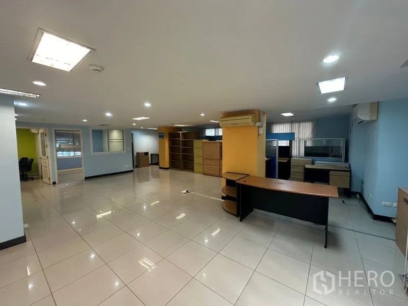 Office Space for sale - Open-plan office area with desks, yellow columns and overhead lighting.
