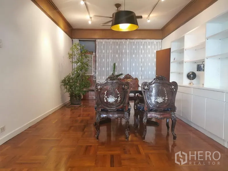 Apartment for rent in Khlong Toei, Bangkok - Formal dining space with carved wooden chairs, black pendant light and potted tree.