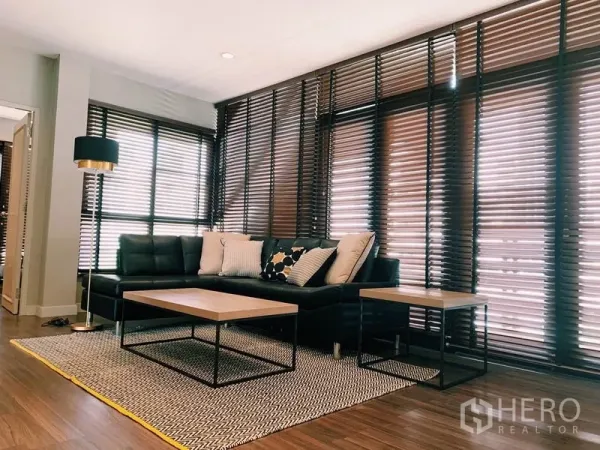 Condominium for rent in Watthana, Bangkok - Cozy living area with an L-shaped leather sofa, coffee tables, rug, and layered blinds.