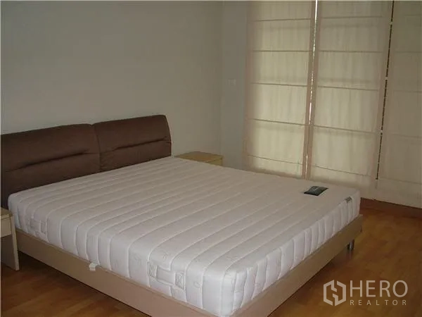 Condominium for rent in Khlong Toei, Bangkok - Master bedroom with king-size bed, wood flooring, and full-height window shades.