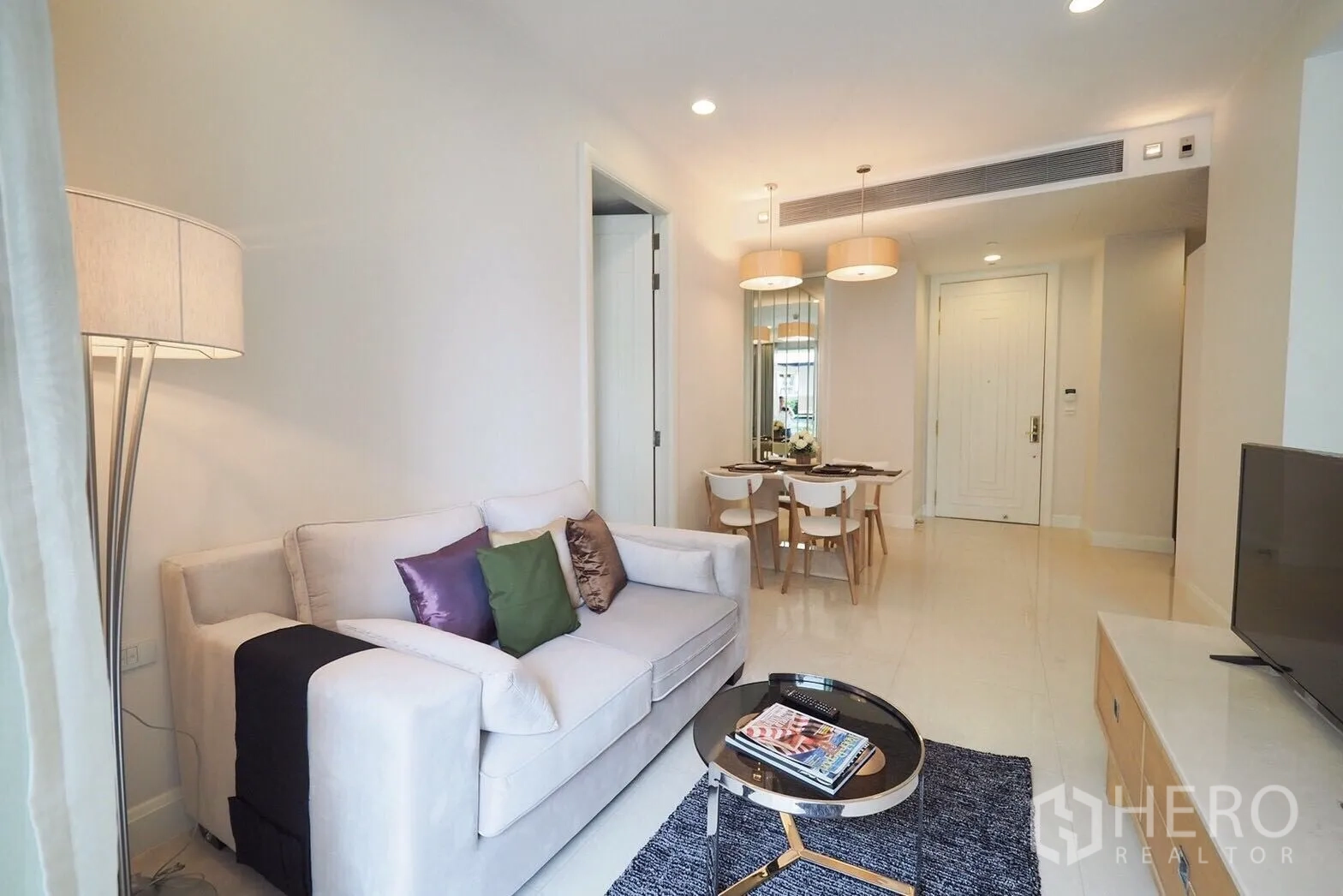 Condominium for rent in Pathum Wan, Bangkok - Cozy living room with sofa, colorful cushions, round coffee table and TV console.