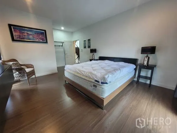 Detached House for rent or sale in Prawet, Bangkok - Spacious master bedroom with wood flooring, bed and bedside tables.
