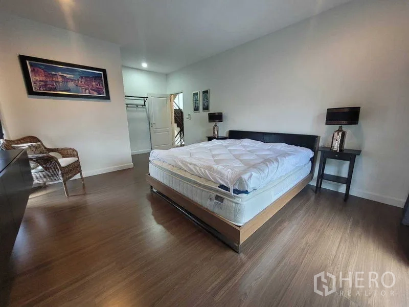 Detached House for rent or sale in Prawet, Bangkok - Spacious master bedroom with wood flooring, bed and bedside tables.