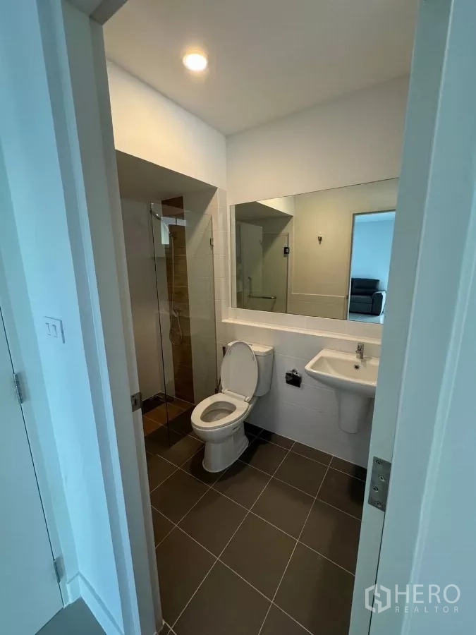 Detached House for rent in Bang Phli, Samut Prakan - Ground-floor bathroom with glass shower enclosure, large mirror and dark floor tiles.