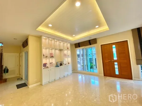Detached House for sale in Khan Na Yao, Bangkok - Bright living area with marble floors, recessed ceiling lights, built-in display shelves, and wooden double doors.
