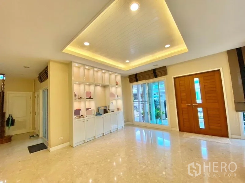 Detached House for sale in Khan Na Yao, Bangkok - Bright living area with marble floors, recessed ceiling lights, built-in display shelves, and wooden double doors.
