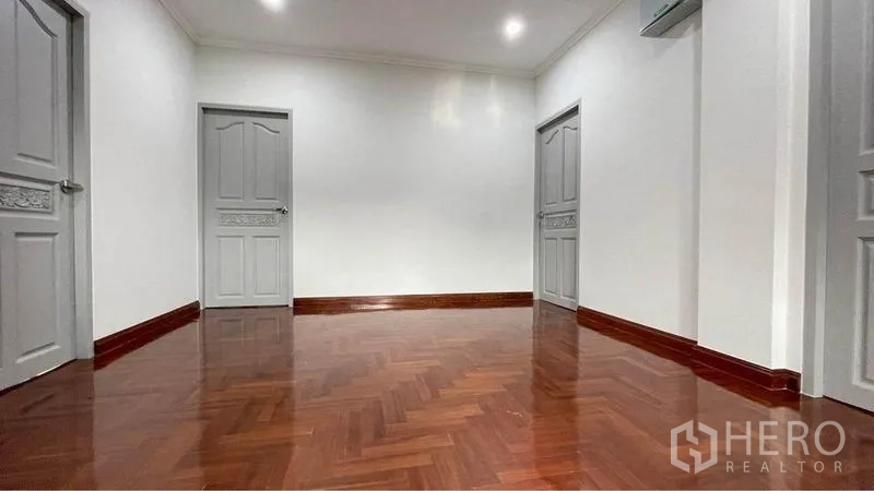 Detached House for rent in Bang Kapi, Bangkok - Bright upstairs landing with herringbone wood floor, white walls and three gray paneled doors.