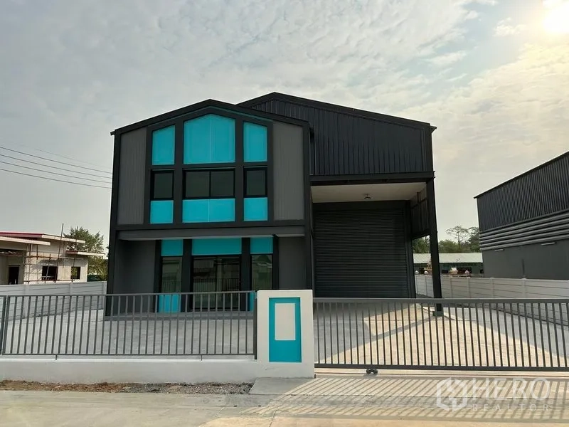 Factory for rent or sale in Bang Bua Thong, Nonthaburi - Front view of a modern mini factory with teal-accented two‑storey office and wide roller shutter in a gated yard.