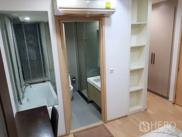 Condominium for rent in Khlong Toei, Bangkok - Hallway view to a bathroom with vanity, toilet and a separate bathtub behind window blinds.