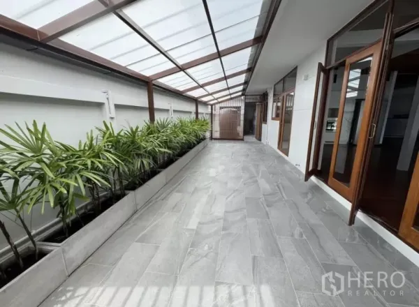 独立式住宅 出租在Watthana, Bangkok - 采光顶覆盖的长廊，灰色地砖与热带绿植花槽。