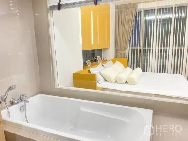 公寓 出租在Watthana, Bangkok - 白色浴缸与大玻璃隔断，可望向温馨卧室与百叶帘