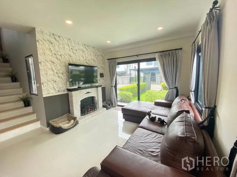 Detached House for rent in Bang Phli, Samut Prakan - Living room with marble‑style TV wall, large sliding doors and brown leather sectional sofa.