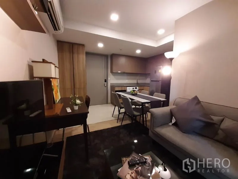 公寓 出租或出售在Watthana, Bangkok - 开放式起居区，沙发、电视、餐桌与后方厨房一体布局。