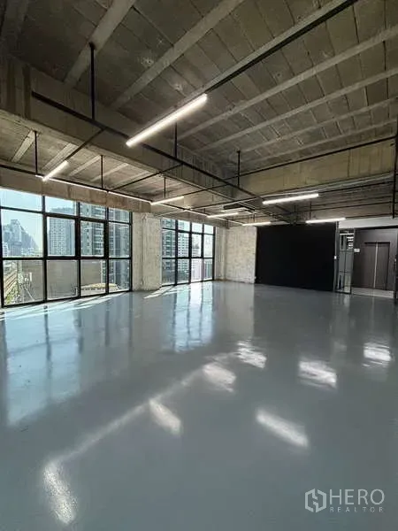 Office Space for rent - Open-plan office with exposed concrete ceiling, linear LED lights and large windows.