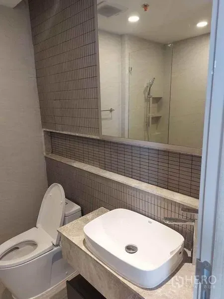 คอนโด ขายในPathum Wan, Bangkok - ห้องน้ำสมัยใหม่ อ่างล้างหน้าวางบนเคาน์เตอร์ กระจกแนวยาว โถสุขภัณฑ์ และผนังกระเบื้อง