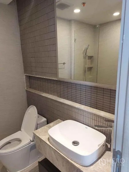 คอนโด ขายในPathum Wan, Bangkok - ห้องน้ำสมัยใหม่ อ่างล้างหน้าวางบนเคาน์เตอร์ กระจกแนวยาว โถสุขภัณฑ์ และผนังกระเบื้อง