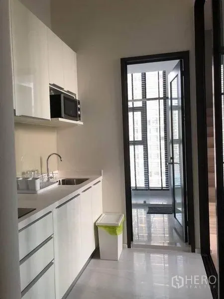 公寓 出售在Ratchathewi, Bangkok - 白色一字型厨房，带水槽与微波炉，连接玻璃阳台空间。