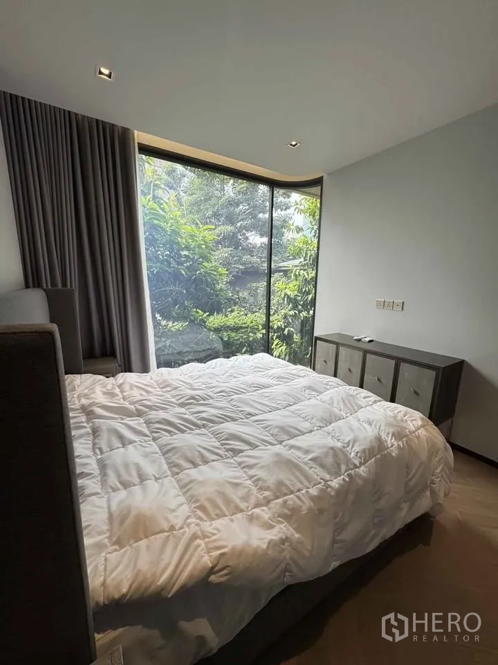 公寓 for rent in Watthana, Bangkok - 卧室配大床与矮柜，落地窗外是浓密绿景。