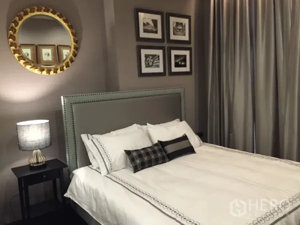 Condominium for rent in Watthana, Bangkok - Stylish Phrom Phong condo bedroom with upholstered headboard, wall art, round mirror and soft lighting.