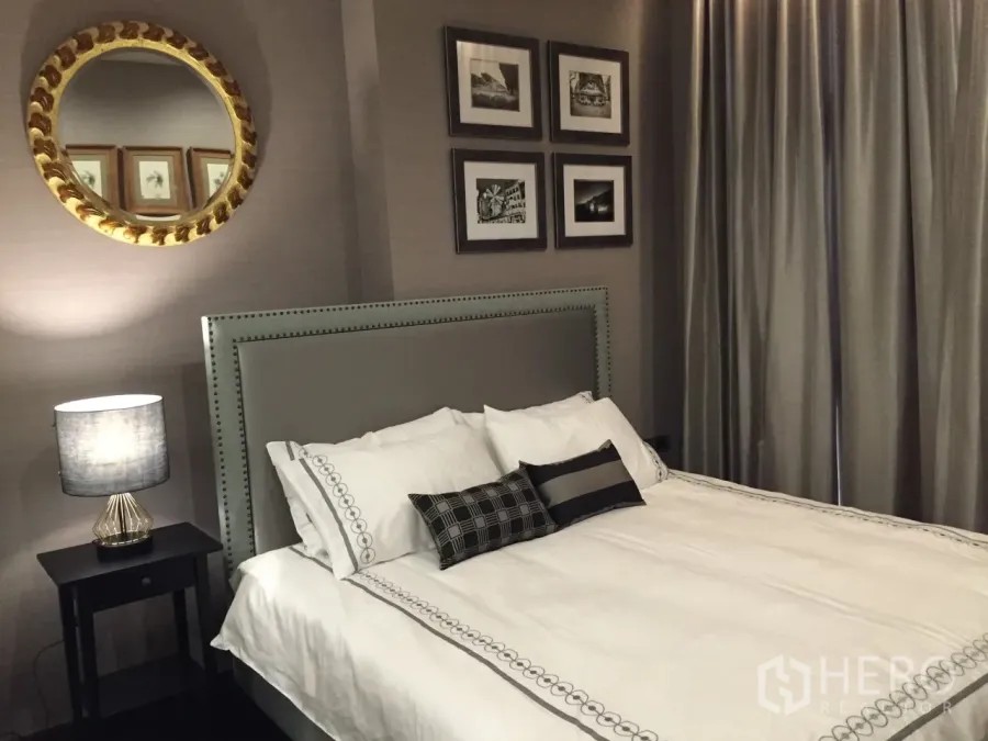 Condominium for rent in Watthana, Bangkok - Stylish Phrom Phong condo bedroom with upholstered headboard, wall art, round mirror and soft lighting.