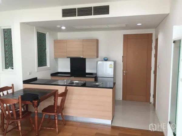 公寓 出租或出售在Watthana, Bangkok - 开放式厨房，浅木色橱柜、黑色台面，配餐桌与冰箱。