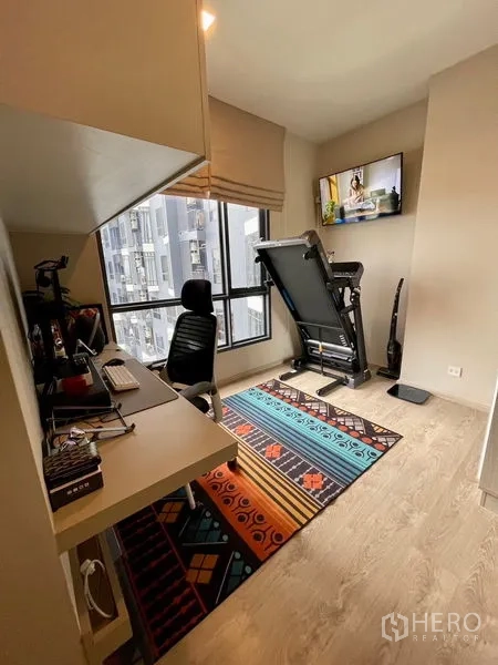 Condominium for sale - Home office and exercise corner with wall-mounted TV, desk and large window.