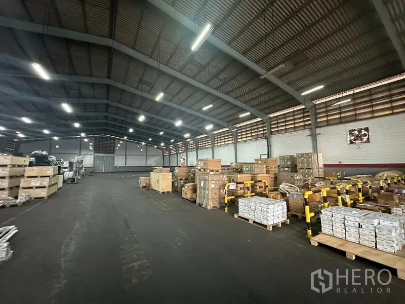 货栈 出租在Khlong Toei, Bangkok - 通风良好的仓库中央通道，托盘与箱货在明亮灯光下排列。