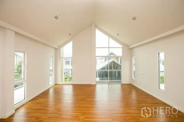 Detached House for rent or sale in Lam Luk Ka, Pathum Thani - Living room with symmetrical gable windows and wide glazing overlooking the estate.