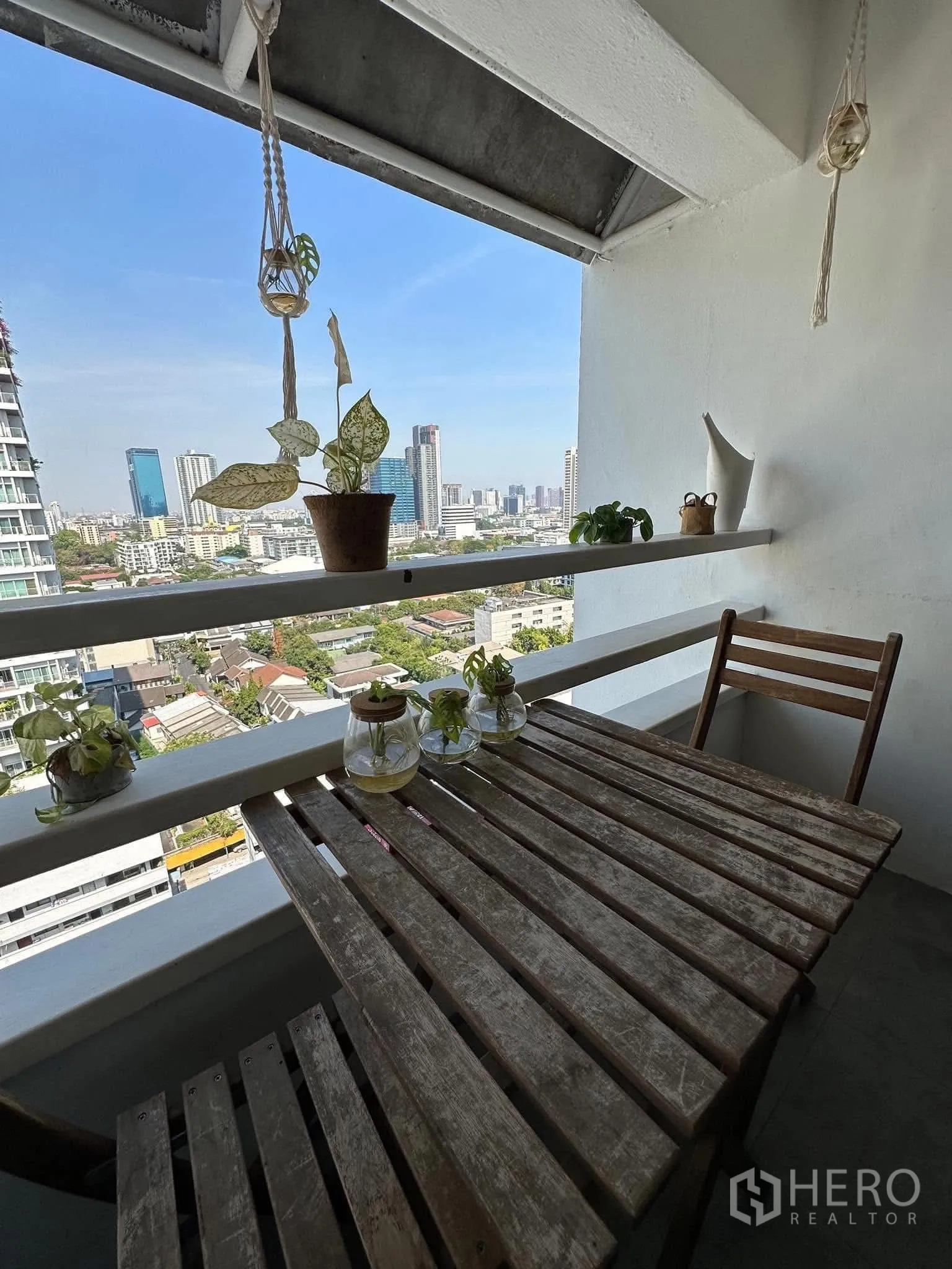 公寓 出租在Watthana, Bangkok - 有顶阳台，木质小餐桌、吊盆植物与开阔城市景观。