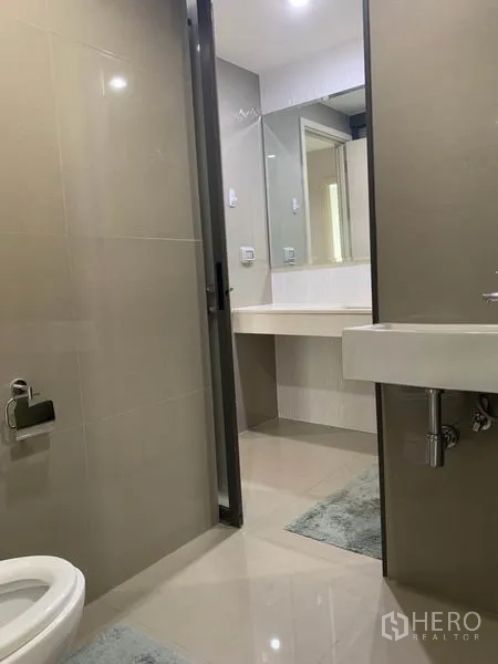 Condominium for rent in Khlong Toei, Bangkok - Tiled bathroom with separate toilet area leading to a large mirror and sink.