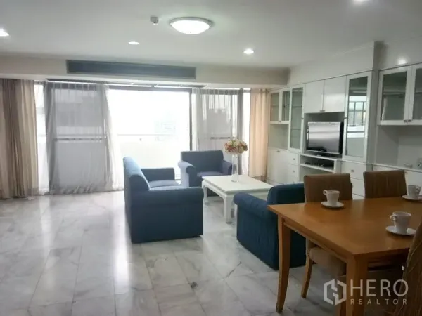 Condominium for rent in Watthana, Bangkok - Bright living room with blue sofas, marble floor, built-in wall unit and balcony windows.