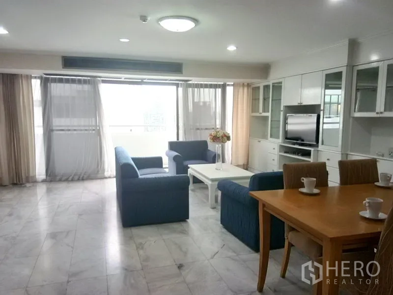 Condominium for rent in Watthana, Bangkok - Bright living room with blue sofas, marble floor, built-in wall unit and balcony windows.