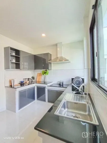 独立式住宅 出售在Wang Thonglang, Bangkok - 明亮的L形厨房，带窗户、不锈钢水槽、抽油烟机与亮面柜体。