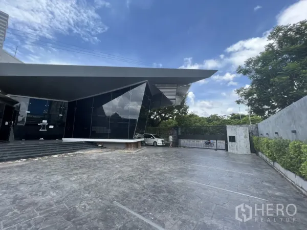 零售空间 出租在Sathon, Bangkok - 现代黑玻璃零售建筑，宽阔前院与铁门车道，蓝天背景。