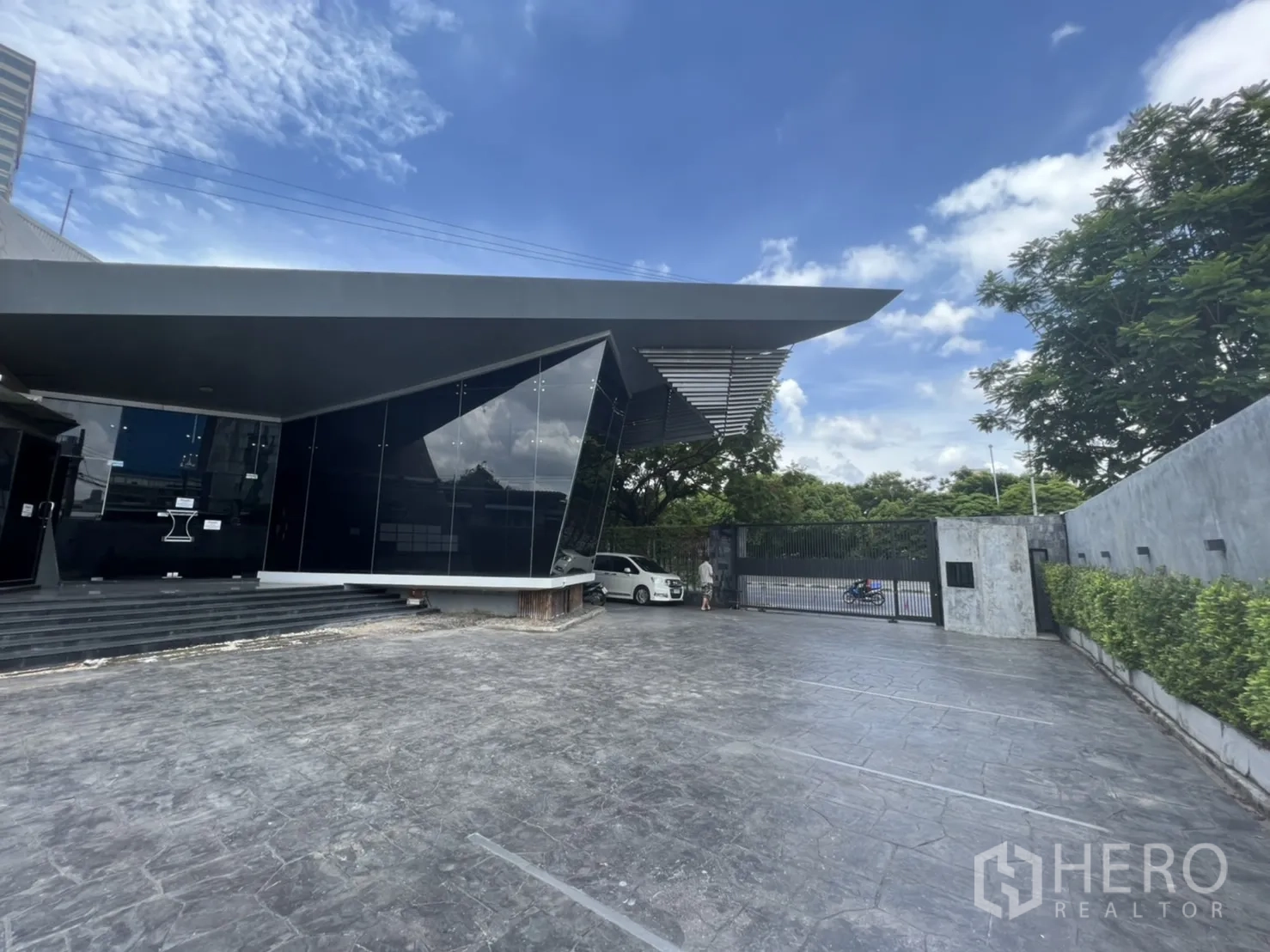 Retail Space for rent in Sathon, Bangkok - Modern black-glass retail building with a wide forecourt and gated driveway under a blue sky.