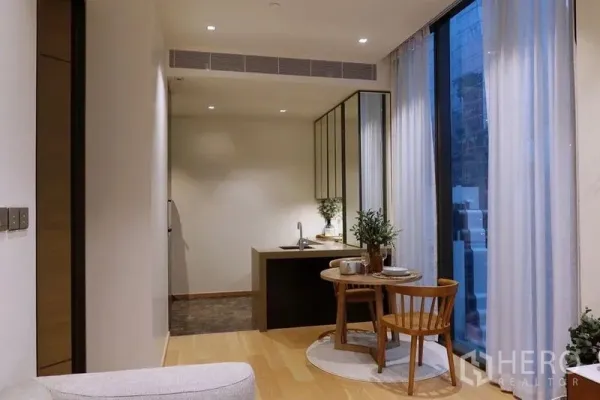 Condominium for rent in Pathum Wan, Bangkok - Open-plan dining and kitchen area with tall windows, wood floors and a round table with two chairs.