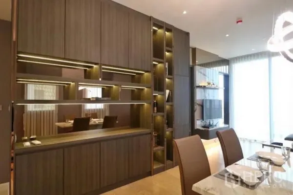 公寓 出租在Khlong San, Bangkok - 带灯光的木质一体柜与展示层架，餐区和大窗客厅相连。