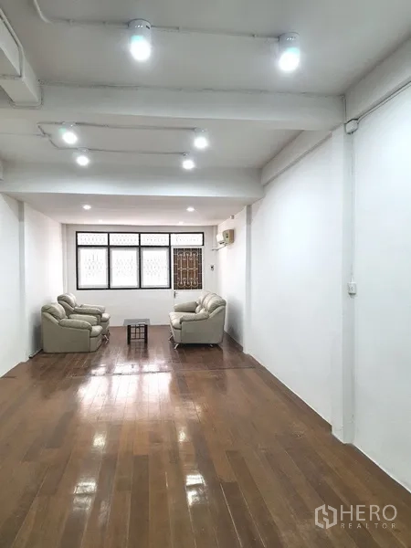 Shophouse for rent in Phra Khanong, Bangkok - Large upper-floor room with wooden flooring, sofas, and wide windows for natural light.