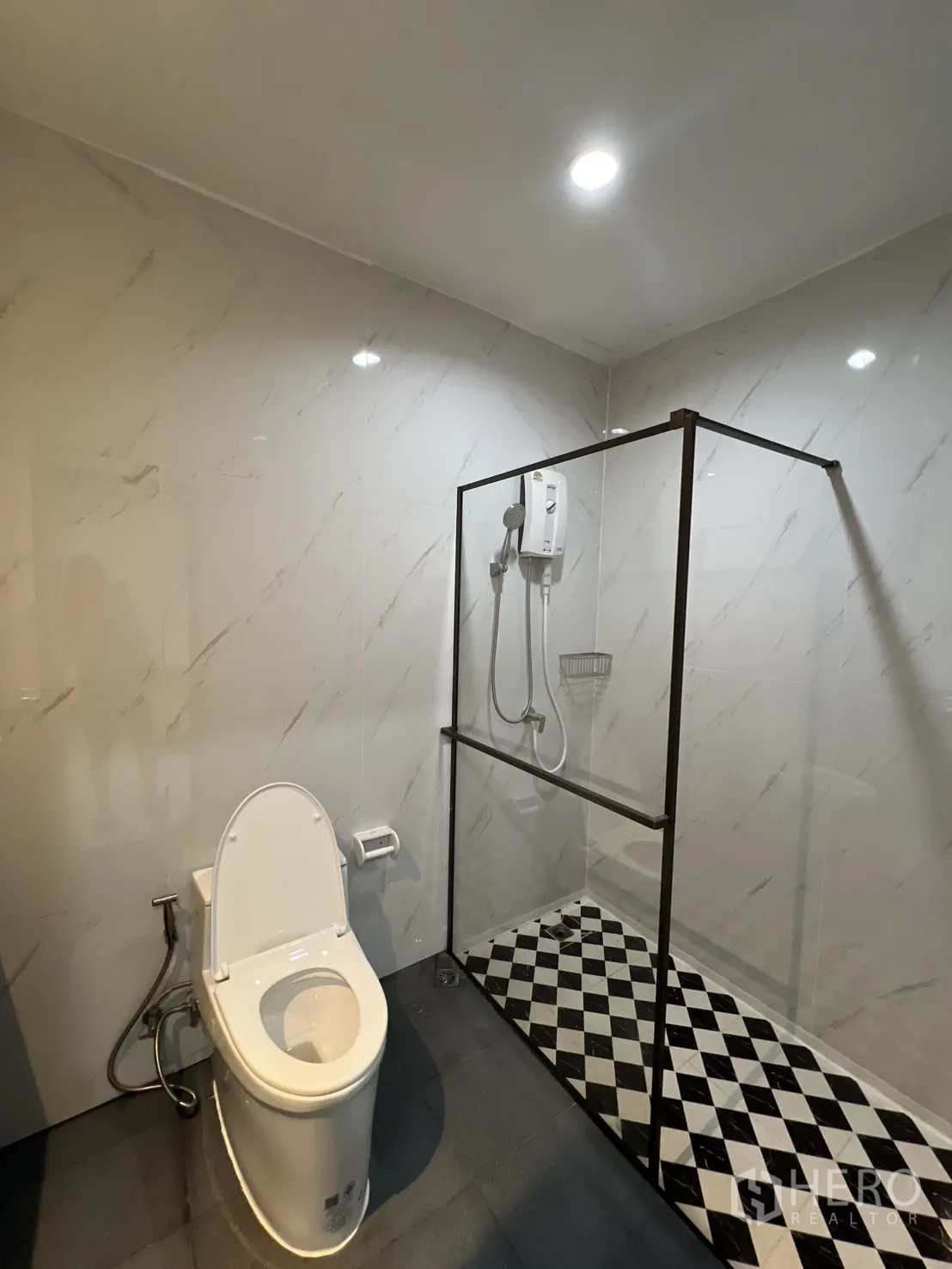 联排别墅 for rent in Watthana, Bangkok - 卫浴配玻璃淋浴间与棋盘格地面，旁有坐便。