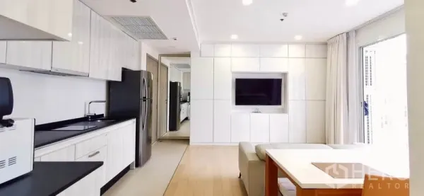 公寓 出租或出售在Watthana, Bangkok - 开放式客厅，内置电视墙、小厨房与餐桌。