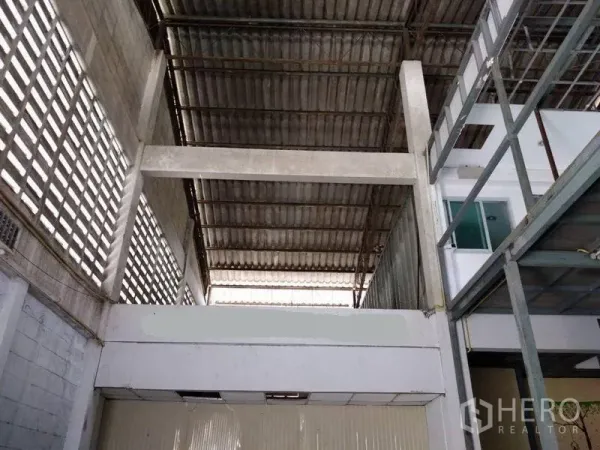 Warehouse for rent in Mueang Nonthaburi, Nonthaburi - High-ceiling warehouse with ventilated block walls, corrugated metal roof and mezzanine walkway beside a windowed office.